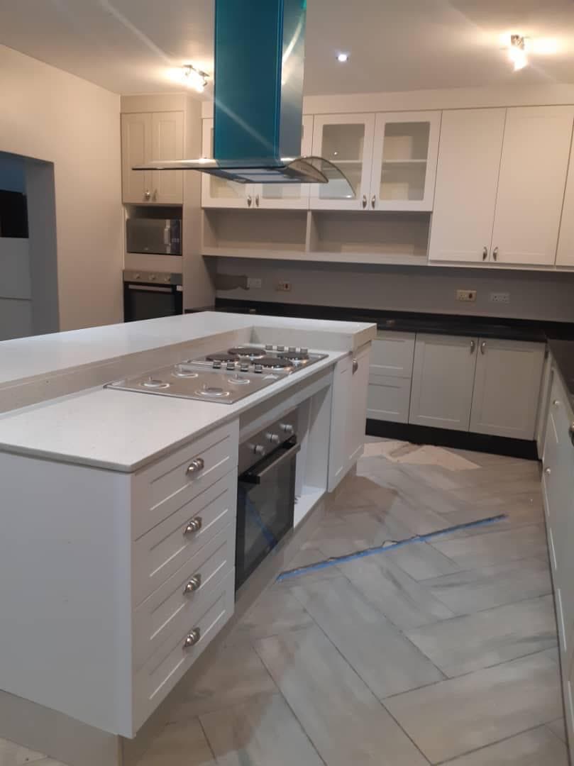 Cream shaker kitchen with a central island, gas hob and glass-fronted wall units.