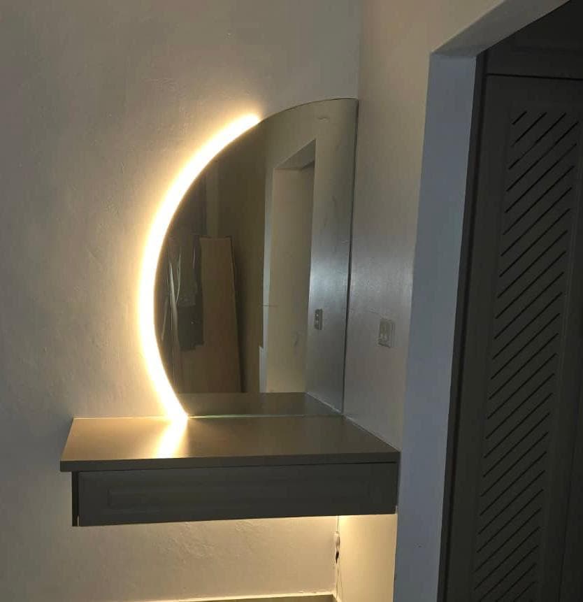 Floating dressing console beneath a backlit half-moon LED mirror.