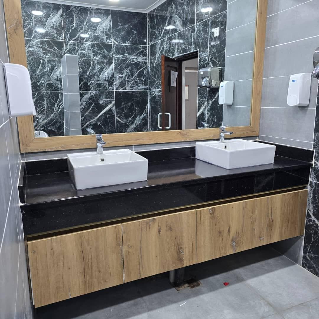 Floating oak vanity with black granite top, twin square basins and a framed mirror.